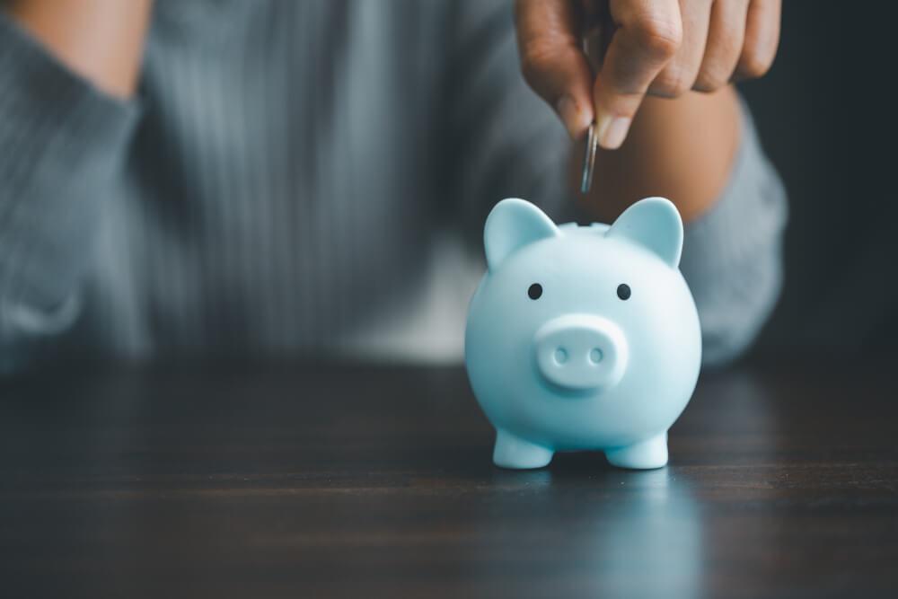 A hand putting a coin into a blue piggy bank.