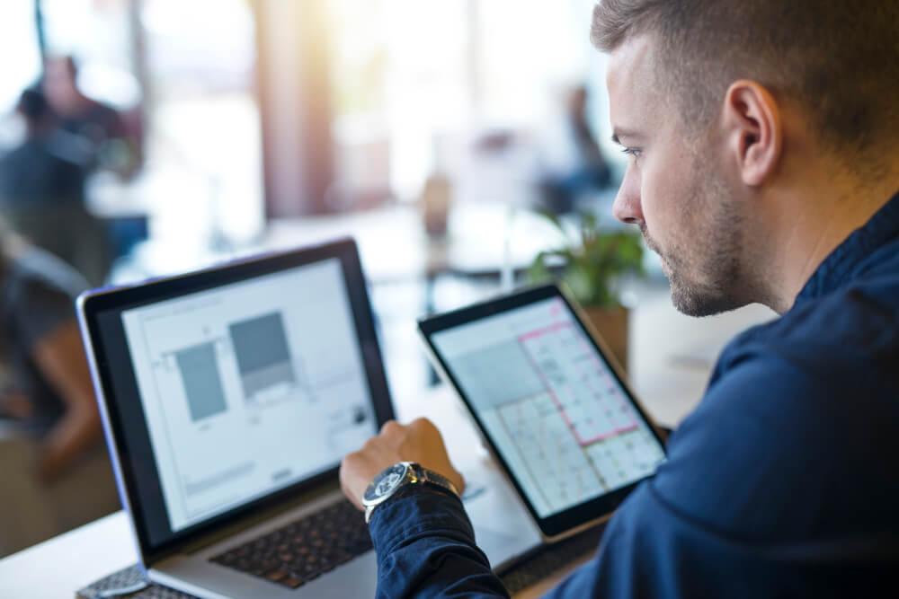 A man working on a laptop computer and a tablet.